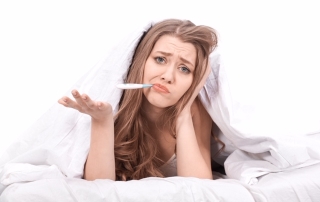 lifestyle shot of sad woman inside her bed checking her temperature and feeling sick.