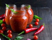 Tomato ketchup sauce with cherry tomatoes and red hot chili peppers, garlic and herbs in a  glass jar on dark background. Homemade tomato sauce and fresh tomatoes