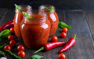 Tomato ketchup sauce with cherry tomatoes and red hot chili peppers, garlic and herbs in a  glass jar on dark background. Homemade tomato sauce and fresh tomatoes